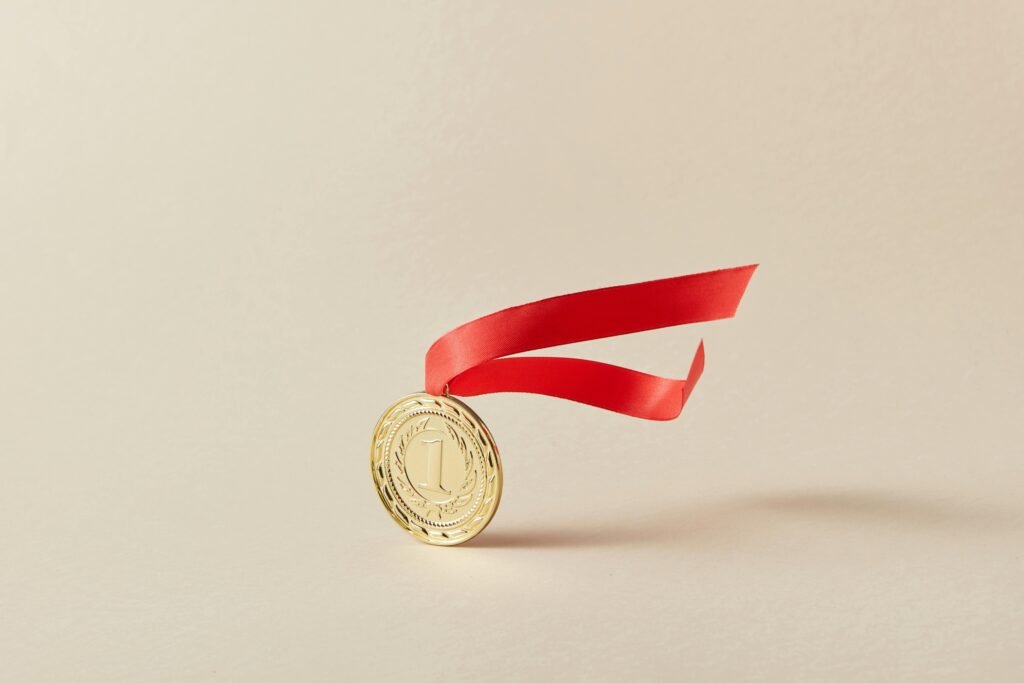 pexels-photo-7267575-7267575 Close-up of a gold medal with a red ribbon against a neutral background.